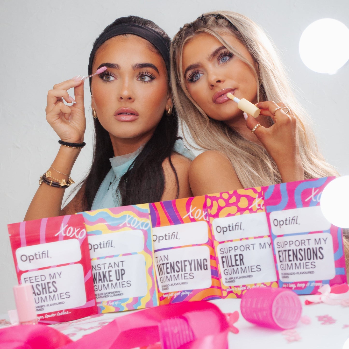 Two women applying makeup with Optifill Gummies on a white table
