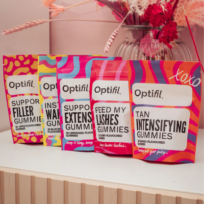 Five colorful Optifil Gummy supplement packages on a shelf with flowers in the background.