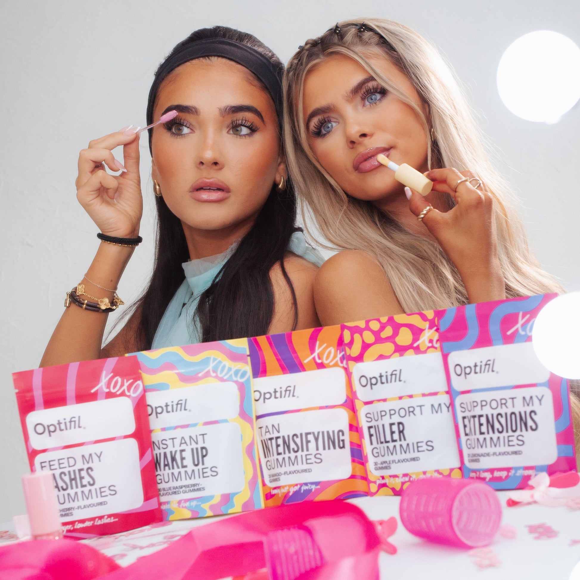 Two women applying makeup with Optifill Gummies on a white table